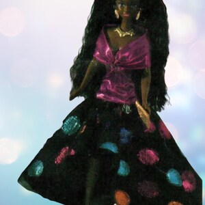 May include: A black doll with long black hair wearing a pink satin top and a black skirt with colourful polka dots.