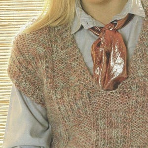 May include: A brown and green knitted vest with a v-neck. The vest is worn over a light blue button-up shirt with a brown satin scarf tied around the collar.