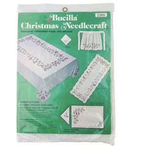 May include: A Bucilla Christmas Needlecraft kit for dinner napkins. The kit includes four 16x16 inch napkins with a "Holiday Garland" design featuring red and green holly, bells, and bows. The kit is labeled "Easy-Care, Permanent Press, Soil Release".