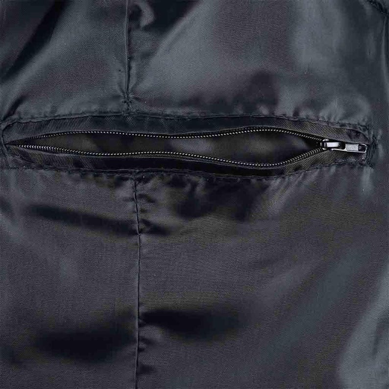 May include: Close-up of a black fabric with a zippered pocket. The pocket is horizontally oriented and sewn into the fabric. The zipper is closed, and the fabric has a slight sheen.