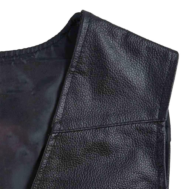 May include: Close-up of a black leather vest. The vest has a textured surface and a V-neck design. The stitching is visible along the seams. The vest appears to be new.