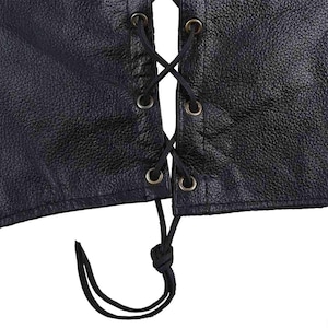 May include: Close-up of a black leather vest with a laced front. The vest features a textured surface and metal grommets. Black lacing is threaded through the grommets in an X pattern, with a knot at the bottom.