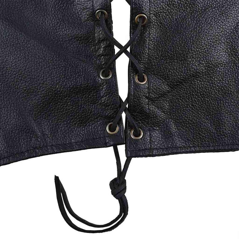 May include: Close-up of a black leather vest with a laced front. The vest features a textured surface and metal grommets. Black lacing is threaded through the grommets in an X pattern, with a knot at the bottom.