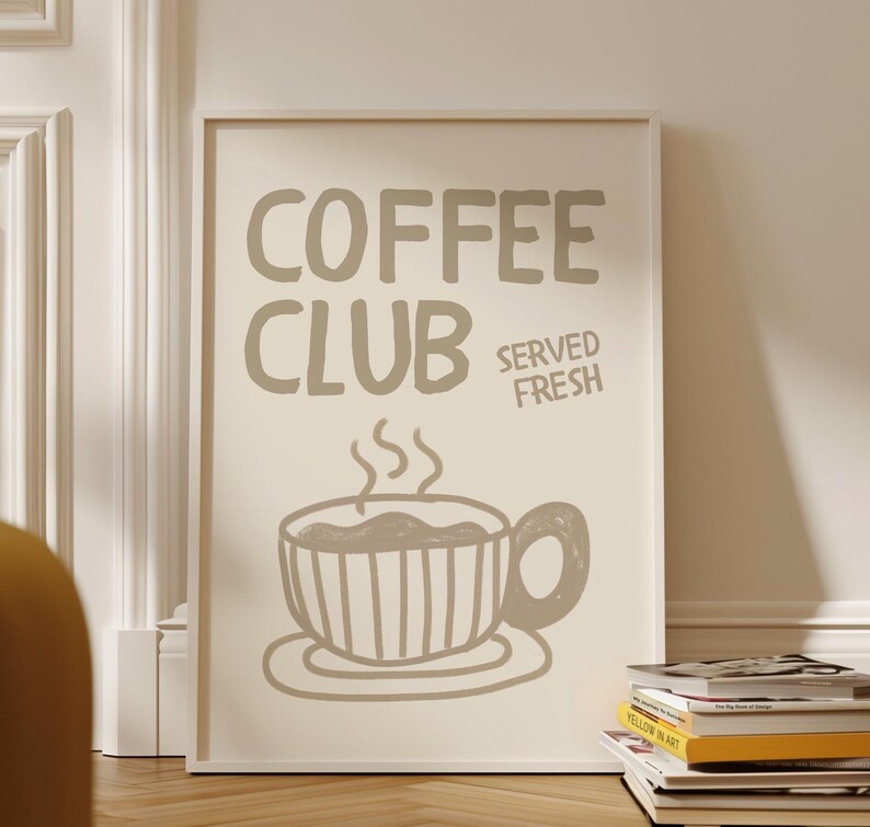May include: A framed poster with the words "COFFEE CLUB SERVED FRESH" in a light brown color. Below the text is a drawing of a coffee cup with steam rising from it. The poster is leaning against a white wall.