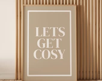 Pode incluir: Uma impressão emoldurada com as palavras "LETS GET COSY" em branco, centradas em um fundo bege. A moldura é de cor castanho claro, e a impressão está encostada em uma parede de madeira com ripas verticais.