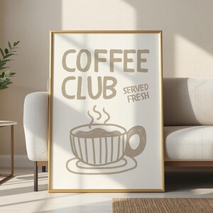May include: A framed print with the words "COFFEE CLUB SERVED FRESH" in brown lettering. The image features a brown coffee cup with steam rising from it. The frame is gold, and the print is displayed against a neutral background.