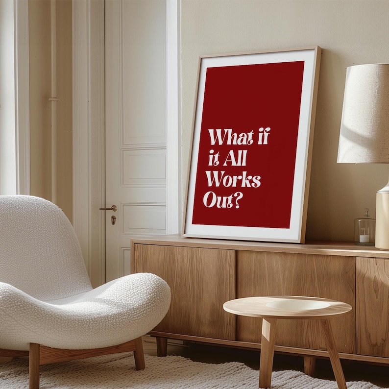 May include: A framed art print with a red background and the white text "What if it All Works Out?" The print is displayed on a wooden cabinet in a room with a white chair and a small wooden table.