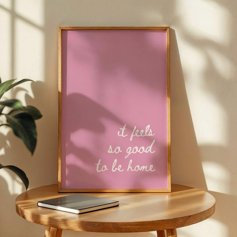 May include: A pink framed print with the text "it feels so good to be home" in white cursive writing.