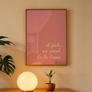 May include: A framed print with a pink background and the text "it feels so good to be home" in white.