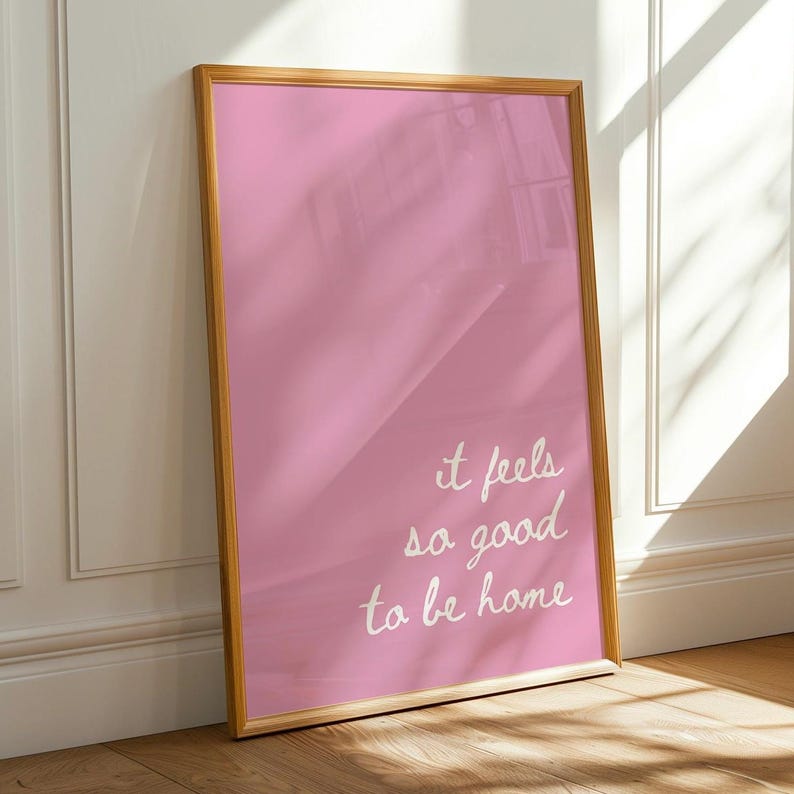 May include: A framed pink poster with white text that reads "it feels so good to be home".