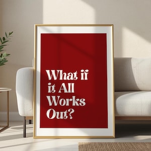 May include: A framed print with a gold border. The print features the text "What if it All Works Out?" in white against a solid red background. The artwork is displayed in a living room setting, leaning against a white sofa.