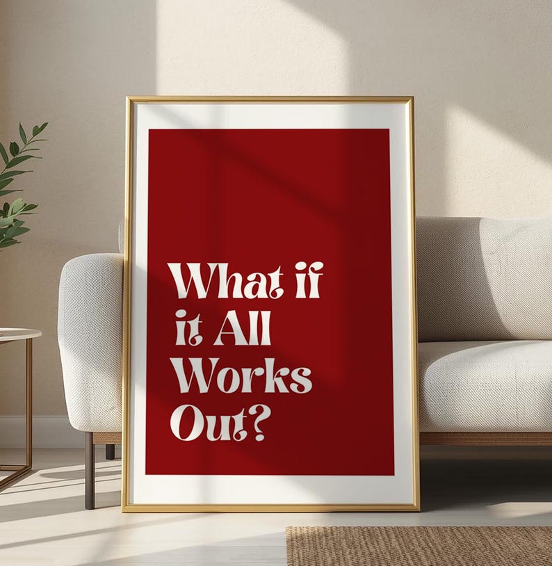 May include: A framed print with a gold border. The print features the text "What if it All Works Out?" in white against a solid red background. The artwork is displayed in a living room setting, leaning against a white sofa.