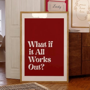 May include: A framed art print with a deep red background and the white text "What if it All Works Out?". The print is in a light wood frame and is displayed in a room with other framed art and wooden furniture.