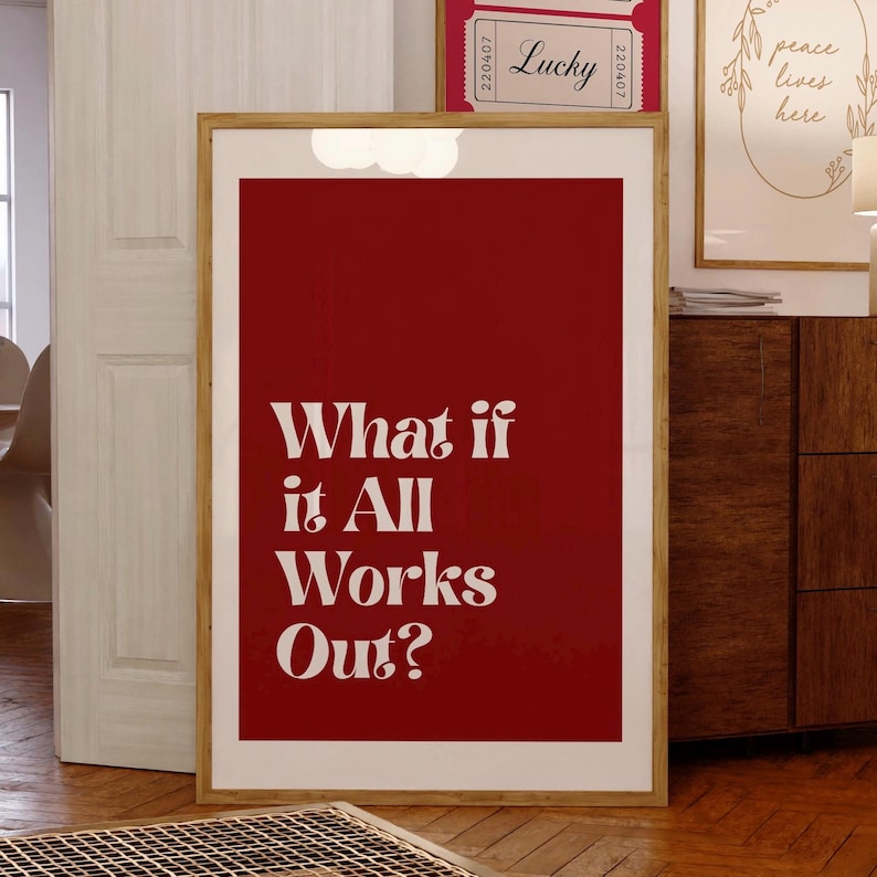May include: A framed art print with a deep red background and the white text "What if it All Works Out?". The print is in a light wood frame and is displayed in a room with other framed art and wooden furniture.