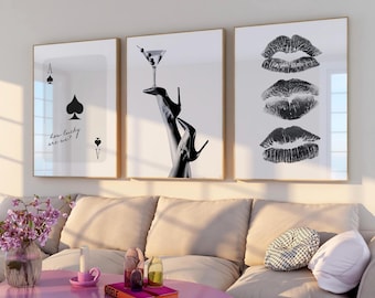 May include: Three framed art prints. The first features a black spade card symbol with the text "how lucky are we?". The second shows a martini glass balanced on high heels. The third displays three lip imprints. All are in black and white.