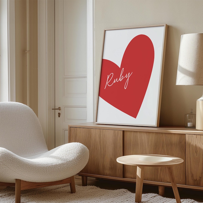May include: A framed art print featuring a large red heart on a white background. The name "Ruby" is written in cursive across the heart. The print is displayed in a light wood frame, adding a touch of warmth to the room.
