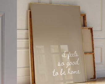 May include: A large beige canvas print with a gold frame. The print features white text that reads "it feels so good to be home".