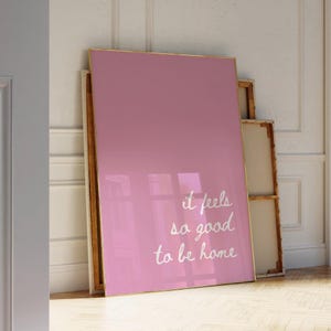 May include: A pink framed poster with white text that reads "it feels so good to be home".