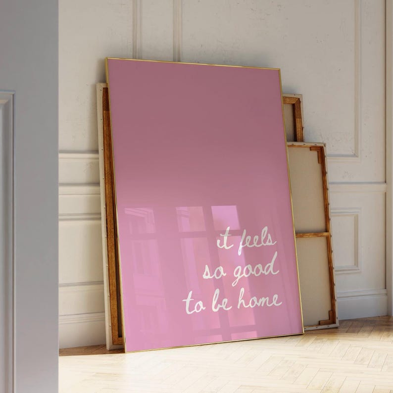 May include: A pink framed poster with white text that reads "it feels so good to be home".