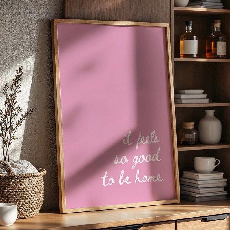 May include: A pink framed poster with the text "it feels so good to be home" written in white cursive script.