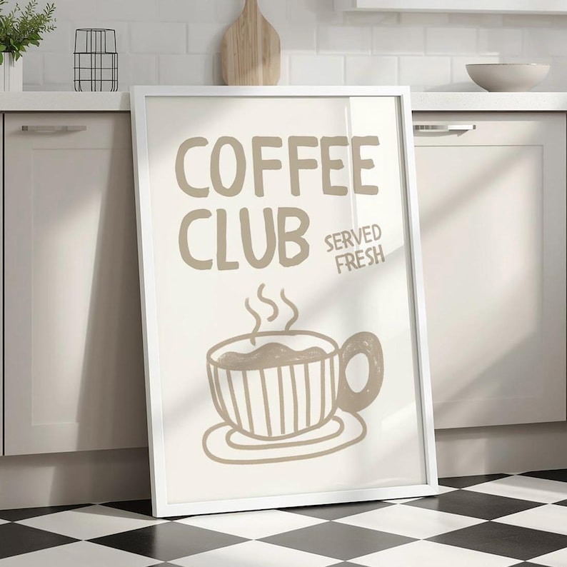 May include: A framed print with the words "COFFEE CLUB SERVED FRESH" in a light brown color. The image features a steaming coffee cup illustration. The frame is white, and the background is a neutral color.
