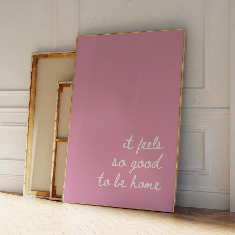 May include: Pink canvas wall art with a gold frame and the text "it feels so good to be home" in white cursive writing.