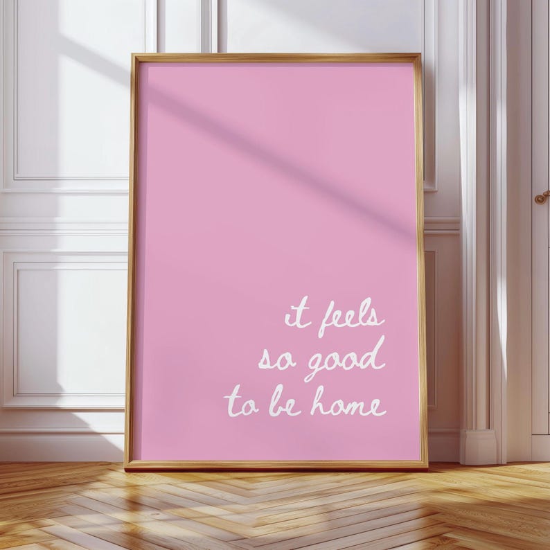 May include: A pink framed poster with the text "it feels so good to be home" in white cursive writing.