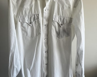 May include: White long-sleeve shirt with a Western style. The shirt has two chest pockets with pointed flaps and snap closures. It features a pointed collar and snap closures down the front and on the cuffs.