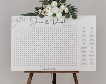 May include: A white wedding sign with black text that says "Jamie & Daniel's Sip and Search". The sign has a word search puzzle with names of people, places, and things related to weddings. The sign is on a wooden easel.