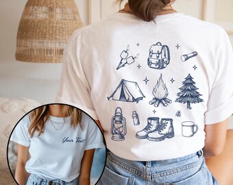 May include: White t-shirt with a blue camping themed design on the back. The design includes a tent, campfire, lantern, backpack, hiking boots, a mug, and a pine tree. The front of the shirt is blank with the text "Your Text" in blue.
