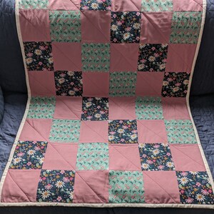 May include: A pink and green floral quilt with a white border. The quilt is made of squares of different floral fabrics.