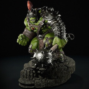 May include: A green Hulk figurine in gladiator armour, holding a spiked mace. The figure is posed on a stone base, with detailed armour and a helmet with a red plume. The background is dark.