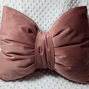 Peut inclure: Un coussin en velours rose poussiéreux en forme de nœud. Le coussin est doux et moelleux, et serait un excellent ajout à tout salon ou chambre à coucher.