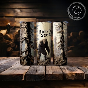 Puede incluir: Tres vasos de acero inoxidable con una escena de bosque y un gráfico de Bigfoot. El vaso del centro tiene el texto "Hide n Seek".