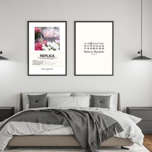 May include: Two black framed prints on a white wall above a bed with a white duvet and a grey and white blanket. The print on the left features a photograph of pink and white flowers with the text "REPLICA" and "Maison Margiela" below. The print on the right features the text "0123456789", "10 11 12 13 14 15 16", "17 18 19 20 21 22 23", "Maison Margiela", and "PARIS".
