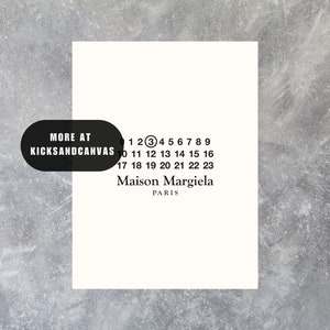 May include: A white card with black text that reads "MORE AT KICKSANDCANVAS" and "1 2 3 4 5 6 7 8 9 10 11 12 13 14 15 16 17 18 19 20 21 22 23 Maison Margiela PARIS".