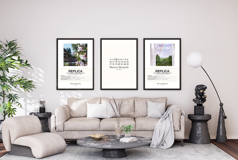 May include: Three framed posters with black frames hanging on a white wall above a beige sofa. The posters feature a floral scene, a white background with black text, and a landscape with a rainbow. The text on the posters reads "REPLICA" and "Maison Margiela Paris".