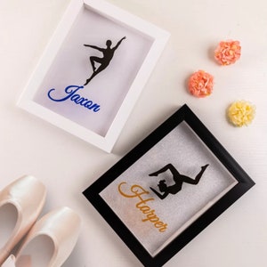 May include: Two white and black shadow boxes with a silhouette of a dancer inside. The white box has the name "Jaxon" in blue lettering and the black box has the name "Harper" in gold lettering.