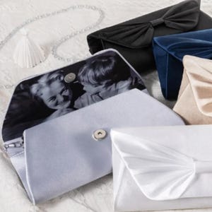 May include: An assortment of satin and velvet clutch purses in various colors, including black, blue, and white. One purse is open, revealing a black and white photograph inside. Some purses feature bow details.