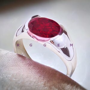 Könnte beinhalten: Ein silberner Ring mit einem großen, ovalen, roten Edelstein.
