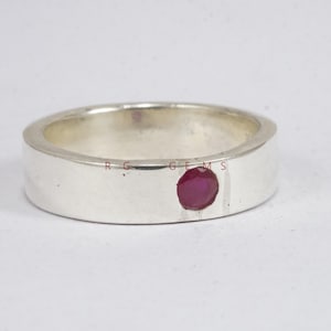 Può includere: Un anello d'argento con una fascia piatta e una singola gemma rotonda di colore rosso intenso. L'anello ha una finitura lucida e un design semplice ed elegante, adatto all'uso quotidiano.