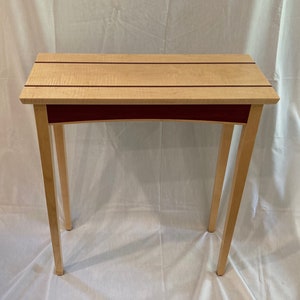 May include: A small, wooden table with a light wood top and dark red accents. The table has four legs and a rectangular top.