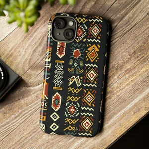 Può includere: Custodia nera per smartphone con un colorato motivo geometrico nei toni del rosso, giallo, verde e bianco. La custodia è realizzata in un materiale resistente ed è progettata per proteggere il telefono da graffi e danni. Mostrata su una superficie di legno.