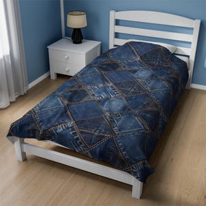 Pode incluir: Um edredom de ganga azul numa estrutura de cama branca. O edredom é feito de retalhos de ganga costurados com costuras douradas visíveis. A cama está num quarto com paredes azuis.