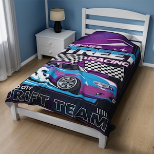 Könnte beinhalten: Eine Bettdecke für ein Einzelbett mit einem auffälligen Design. Sie zeigt ein blaues und lila Sportwagen, Schachflaggen und die Worte "Street Racing" und "Drift Team". Die Decke liegt auf einem weißen Bettrahmen.
