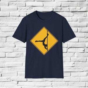 Puede incluir: Camiseta azul marino con un diseño de diamante amarillo que muestra una silueta negra de una persona bailando en barra. El diseño está centrado en la parte delantera. La camiseta está hecha de un material suave y cómodo.