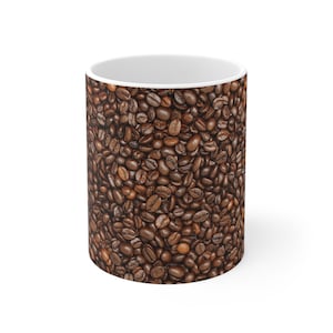 May include: White ceramic coffee mug with a wrap-around design of roasted coffee beans. The beans are various shades of brown, creating a textured appearance. The mug has a white interior and a glossy finish.