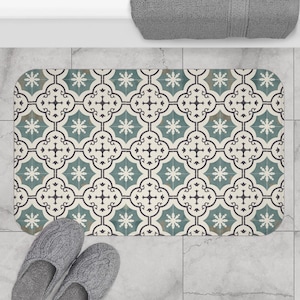 May include: A rectangular bath mat with a repeating pattern of teal, cream, and dark gray floral and geometric shapes. The mat is placed on a light gray tiled floor, with a pair of gray slippers at the bottom.