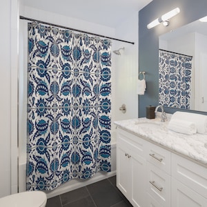 May include: A white shower curtain with a blue and white floral pattern. The shower curtain is hanging in a bathroom with a white vanity and a white tiled shower.