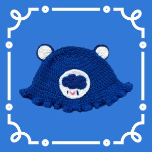 May include: Blue crocheted hat with a white cloud and pink heart design. The hat has a wide brim and is perfect for a casual look.
